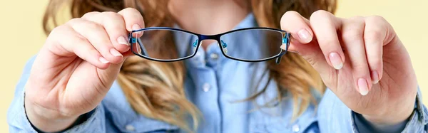 Mujer joven con el pelo de jengibre sosteniendo gafas de lectura delante de ella. Mujer joven con gafas sobre fondo amarillo, pancarta de oftalmología —  Fotos de Stock