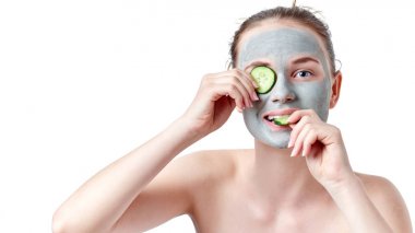 Genç cilt bakım kavramı. İki dilim salatalık, beyaz arka plan üzerinde izole tutarak kuru kil maskesi ile genç genç kız