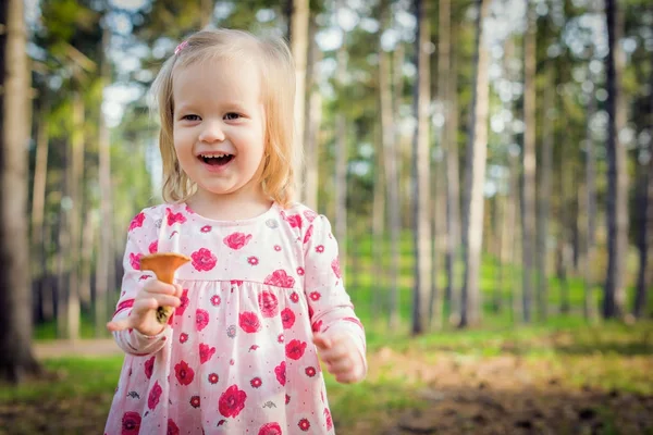 Menina loira bonito da criança colhendo cogumelos em uma floresta. Criança feliz segurando um cogumelo e rindo — Fotografia de Stock