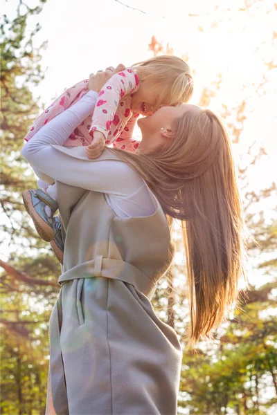 Jovem mãe solteira segurando bonito criança menina filha em seus braços e levantá-la no ar, ambos rindo — Fotografia de Stock