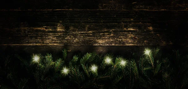 Різдвяний фон, ялинкові гілки з різдвяними вогнями на темному дерев'яному тлі, Святковий прапор з копіювальним простором — стокове фото
