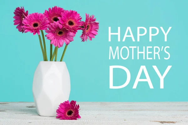 Happy Mother\'s Day Pastel Candy Blue Coloured Background with Dark pink gerberas in a vase.