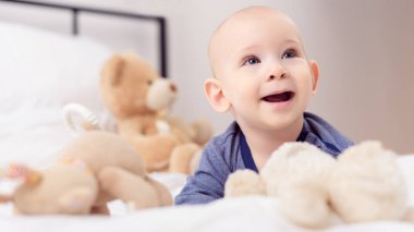 Gülüyor ve oyuncakla oynamak güzel bebek çocuk yatağı üzerinde taşımaktadır. Yeni doğan çocuk yatakta rahatlatıcı. Aile sabah evde.