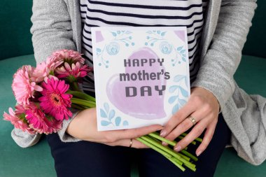 Anneler Günü tebrik kartı bir kanepede oturan ve Gerbera'lardan oluşan tutan unrecognisable genç anne.