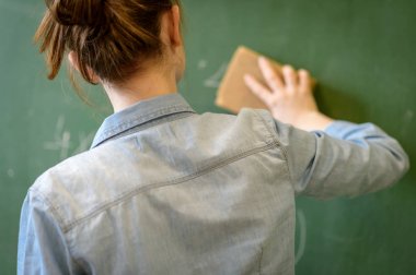 Kadın öğretmen ya da bir öğrenci blackboard bir sünger ile temizlik. Arkadan görünüş.