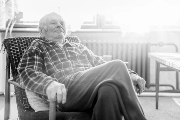 Handsome 80 plus year old senior man portrait. Black and white full body image of elderly man sitting in an armchair in a nursing home.