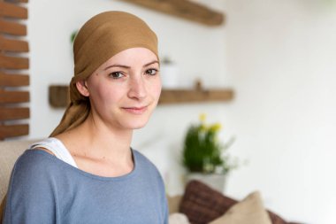 Portrait of young positive adult female cancer patient sitting in living room, smiling and looking at the camera. clipart