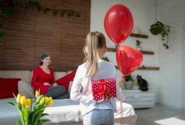 Young mother, cancer patient, and her cute daughter, celebrating return home from hospital. Welcome home or birthday party with balloons and presents. clipart