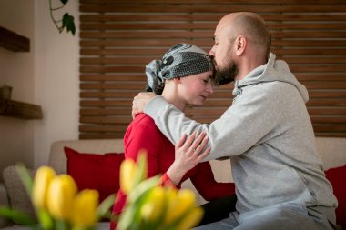 Supportive husband kissing his wife, cancer patient, after treatment in hospital. Cancer and family support concept. clipart