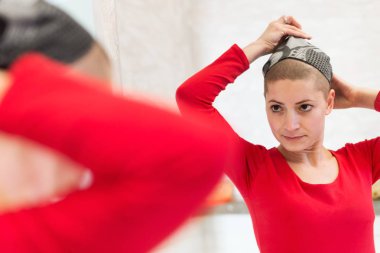 Young adult female cancer patient adjusting her headscarf looking in the mirror. Tired, exhausted, depressed and scared cancer patient. clipart