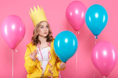 Komik kavramsal fotoğrafçılık. Doğum günü balonları pop gibi davranarak iğne tutan doğum günü şapkalı arsız kız. Çekici trendy genç kutluyor doğum günü.