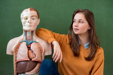 Bir yapay insan vücudu modeli ile serin kadın yüksek okul öğrenci portresi. Öğrenci biyoloji dersinde eğleniyor. Eğitim kavramı.