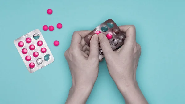 パステル ブルーの背景にピンクの錠剤でブリスター パックを保持している女性の手のクローズ アップ 薬を病気の患者の服用 — ストック写真