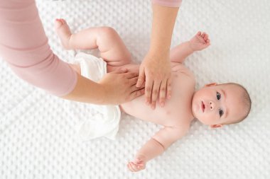 Bebek masajı. Kadın terapist, yeni doğmuş bebeğe nazikçe masaj yapıyor. Anne, yeni doğmuş bebeğine vücut losyonu sürüyor. Yeni doğan masaj üst görünüm arka planı.