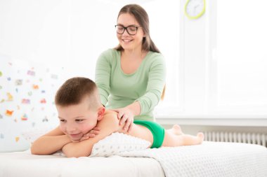 Çocuk masajı konsepti. Genç bayan masaj terapisti 6 yaşındaki bir çocuğa sırt masajı yapıyor. Fizik tedavi.