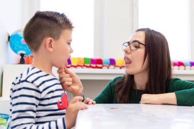 Çocuk konuşma terapisi konsepti. Anaokulu öğrencisi bir kadın konuşma terapistiyle doğru telaffuz pratiği yapıyor.. 