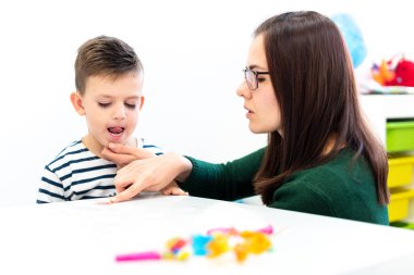Çocuk konuşma terapisi konsepti. Anaokulu öğrencisi bir kadın konuşma terapistiyle doğru telaffuz pratiği yapıyor..