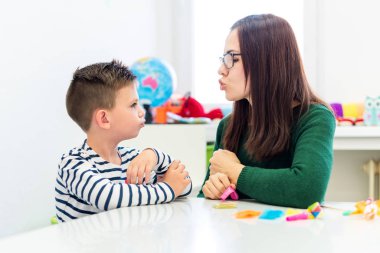 Çocuk konuşma terapisi konsepti. Anaokulu öğrencisi bir kadın konuşma terapistiyle doğru telaffuz pratiği yapıyor..