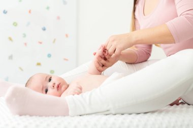 Bebek masajı geçmişi. Anne oğluna nazikçe masaj yapıyor. Bebek sırt üstü uzanıyor ve masaj sırasında kameraya bakıyor..