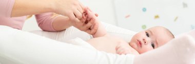 Bebek masaj afişi. Anne, oğluna nazikçe masaj yapıyor ve cildine vücut losyonu sürüyor. Bebek sırtüstü uzanıp kameraya bakıyor.