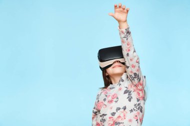 Pastel mavi arka planda sanal gerçeklik gözlüğü takan beyaz bir kızın stüdyo portresi. Gelecekteki cihazlar teknoloji konsepti.