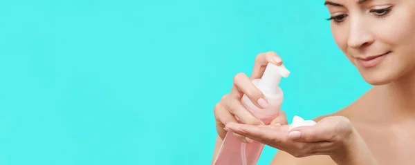 Young woman using gentle foam facial cleanser. Photo of an attractive caucasian woman with healthy skin isolated on turquoise background washing her face with foam soap.