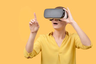 Sanal gerçeklik gözlüğü kullanan 30 'lu yaşlardaki genç bir kadın. Sarı arka planda VR gözlük takan kadın. VR deneyim kavramı.