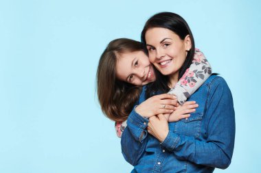Annesini kucaklayan sevimli ve oyuncu bir kızın stüdyo portresi. Mutlu gülümseyen aile geçmişi beyaz arka planda izole edilmiş..
