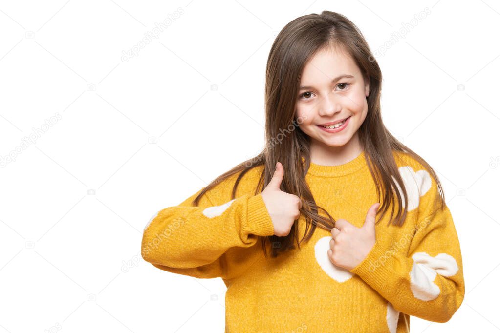 Studio portrait of a young girl on white background giving thumbs up while smiling and looking at camera. Ok sign, satisfaction, success, agreement concept.