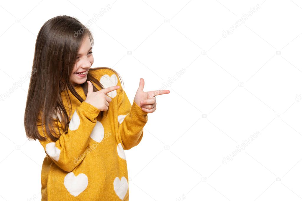 Beautiful young girl in mustard yellow sweater llaughing while pointing to the side. Waist up studio shot on white background.