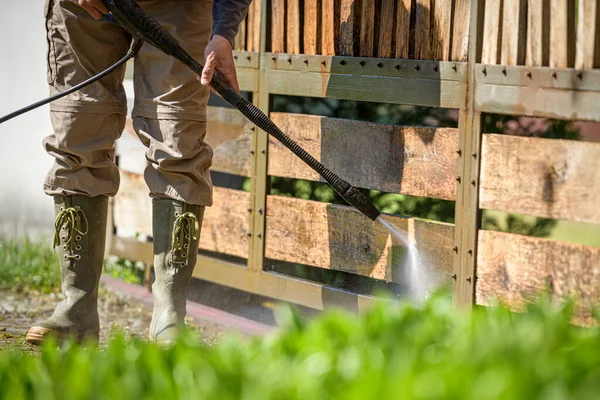 Unrecognizable man cleaning a wooden gate with a power washer. High water pressure cleaner  used to DIY repair garden gate.