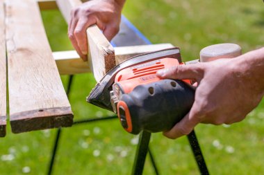 Bahçede tahtaları zımparalayarak tanınmaz hale gelen bir adam. DIY ev geliştirme, restorasyon, marangozluk konsepti. Detaylı el çekimi.
