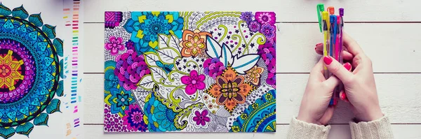 Adult coloring book, stress relieving trend. Art therapy, mental health, creativity and mindfulness concept. Flat lay close up on woman hands coloring an adult coloring book banner.