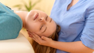 Female physiotherapist or a chiropractor adjusting patients neck. Physiotherapy, rehabilitation concept. Side view cropped shot.