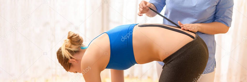 Physical therapist applying kinesio tape on female patient's lower back. Kinesiology, physical therapy, rehabilitation concept. Cropped shot close up banner.