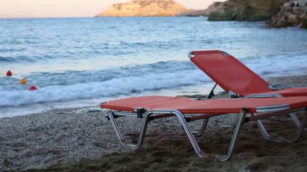 Lege ligbedden staande op een strand door een blauwe zee — Stockvideo