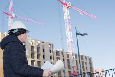 Bir inşaat vinçleri ve elinde planları ile mühendis