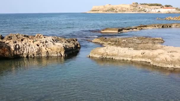 Costa rocosa de un mar azul con antigua fortaleza de Rethymno en el fondo desenfocado — Vídeos de Stock