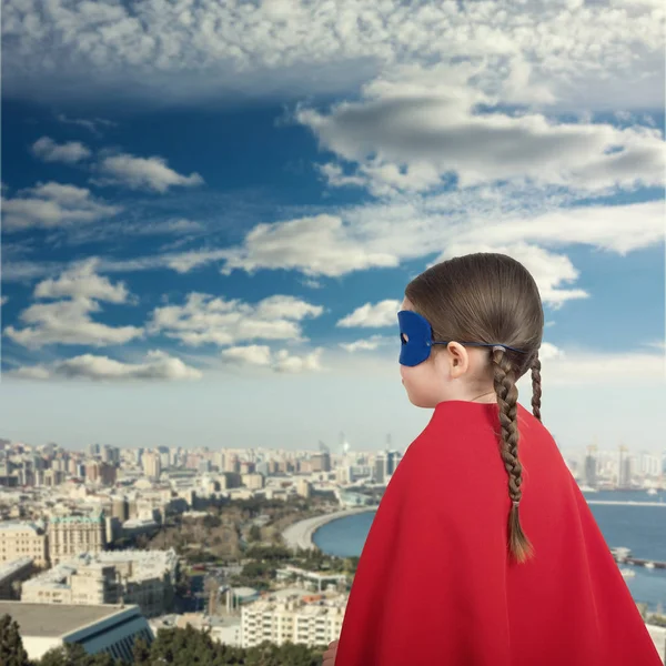 Симпатична дівчинка супергероя в червоному плащі на міському тлі — стокове фото