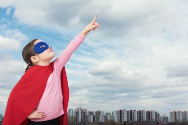 Kentsel arka planı kırmızı pelerin, şirin küçük süper kahraman kız