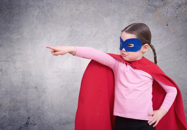 Linda niña super héroe en la capa roja contra la pared gris — Foto de Stock