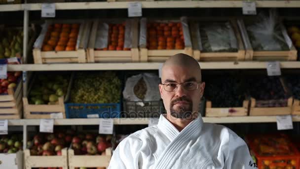 Een man tegen de achtergrond met racks met groenten en fruit — Stockvideo
