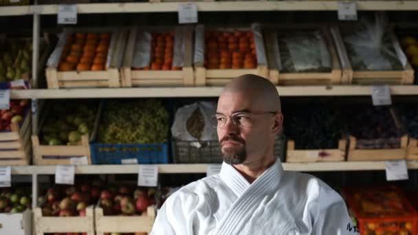 Een man tegen de achtergrond met racks met groenten en fruit — Stockvideo