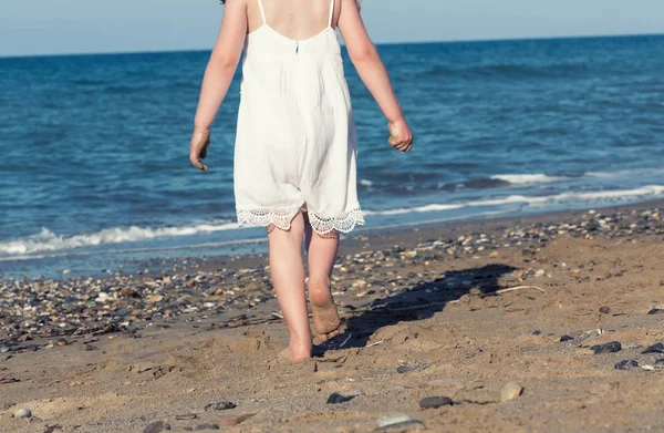 Kleines Mädchen in weißem Kleid, das allein am Meer spaziert und am Ufer spielt — Stockfoto