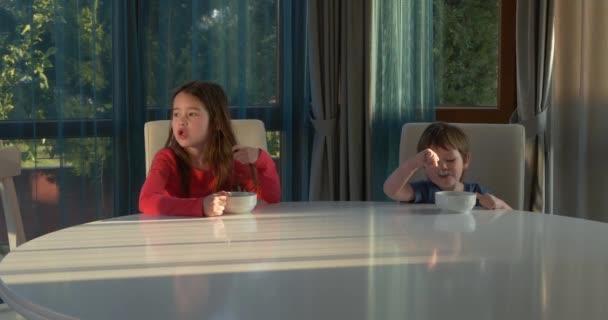 Bambini felici che mangiano corn flakes per colazione. Fratello e sorella hanno fiocchi di mais per la colazione seduti a un tavolo a casa — Video Stock