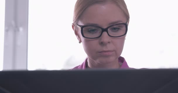 Portret van een lachende vrouw die een bril draagt terwijl ze op een laptop werkt — Stockvideo