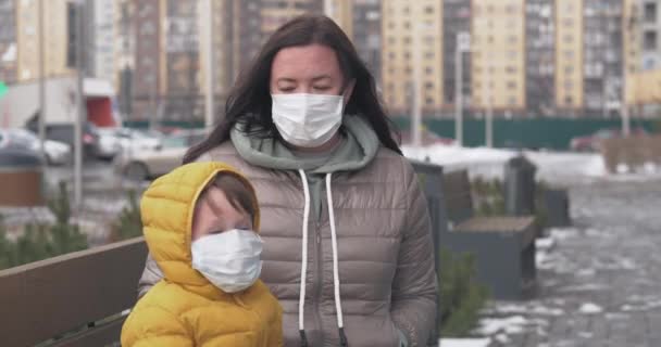 Eine Mutter setzt sich und ihrem kleinen Sohn eine Schutzmaske auf — Stockvideo