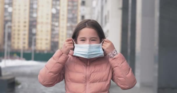 Skydd mot Coronavirus. En kaukasisk flicka sätter på sig en medicinsk skyddsmask stående på en gata — Stockvideo