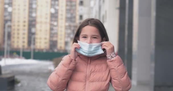 Coronavirusbescherming. Een blank meisje zet een medisch beschermend masker op, staand op straat. — Stockvideo