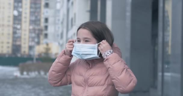Skydd mot Coronavirus. En kaukasisk flicka sätter på sig en medicinsk skyddsmask stående på en gata — Stockvideo